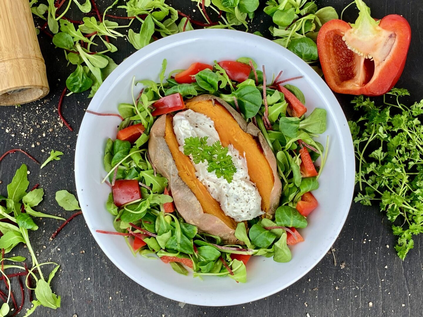 Patate douce rôtie ouverte, garnie d’une sauce blanche et servie sur une salade